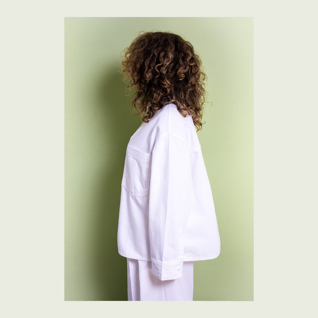 vrouw in witte kleding met krullend haar, tegen groene achtergrond